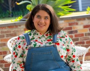 Olivia Muscat - A woman in a colourful shirt and blue overalls sitting in the sun